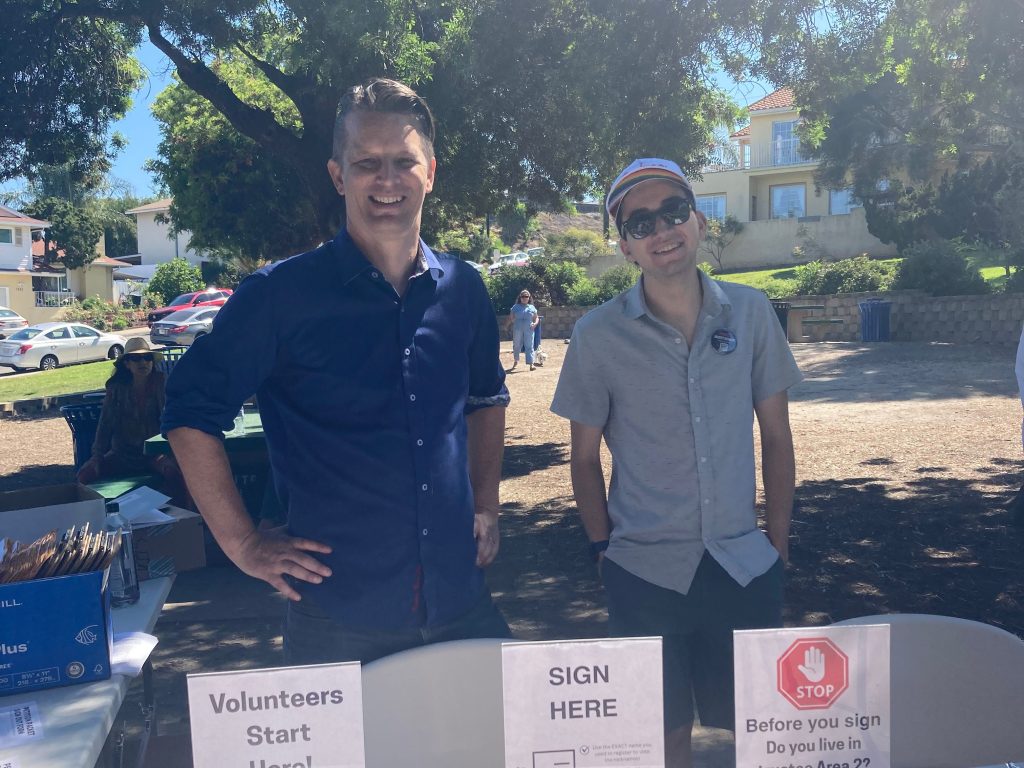 Photo of two Eckert recall volunteers. They are standing outside at a park. They are smiling at the camera